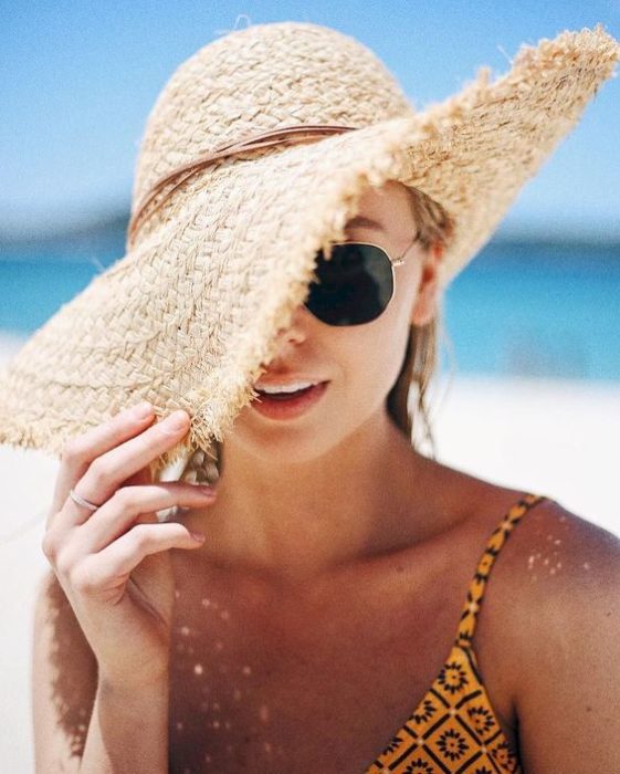 Chica en la playa cubriendo medio rostro con un sombrero 