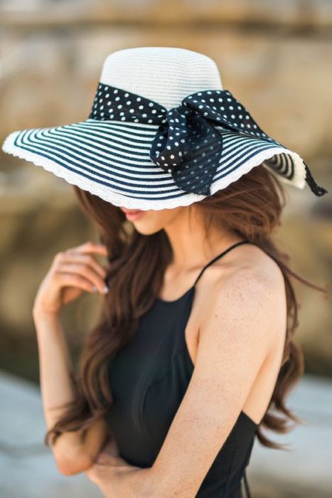 Chica cubriendo su rostro con un sombrero grande a rayas negras