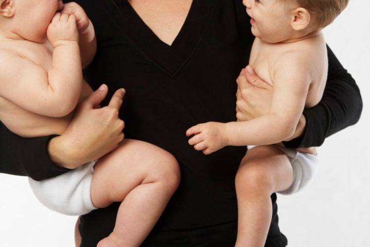 cuerpo de una mujer con blusa negra cargando a dos bebés, uno de cada lado