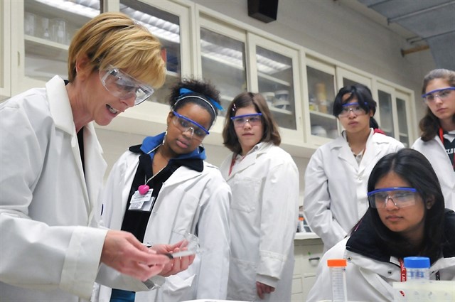 varias mujeres en bata de laboratorio observan algo en un laboratorio