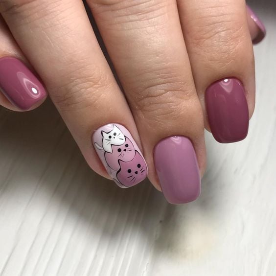Mano de mujer con uñas pintadas en color rosa pastel y fuscia con detalles en gatos pequeños