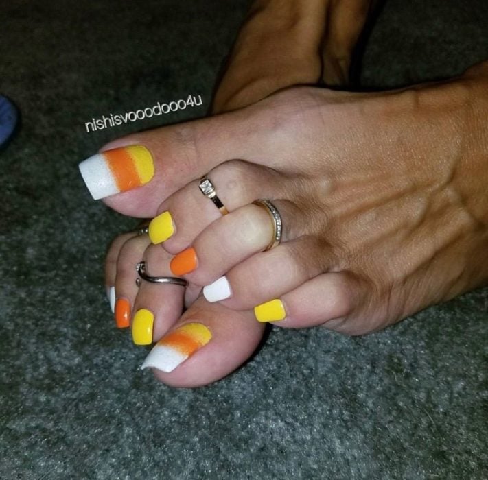 Chica con uñas acrilicas en los pies en color blanco, naranja y amarillo 