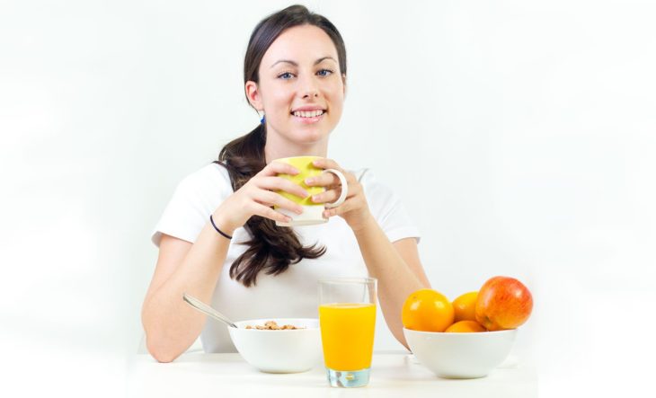 Mujer desayunando jugo, café, naranjas y cereal