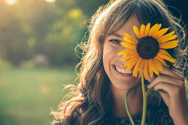 mujer rubia sonriendo con una flor de girasol en la mano 