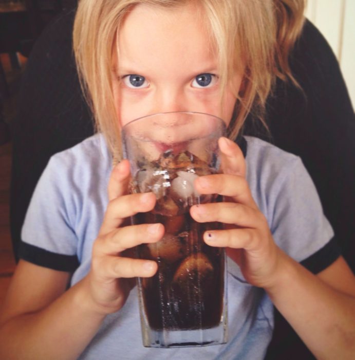 Bambina che beve da un bicchiere di coca cola