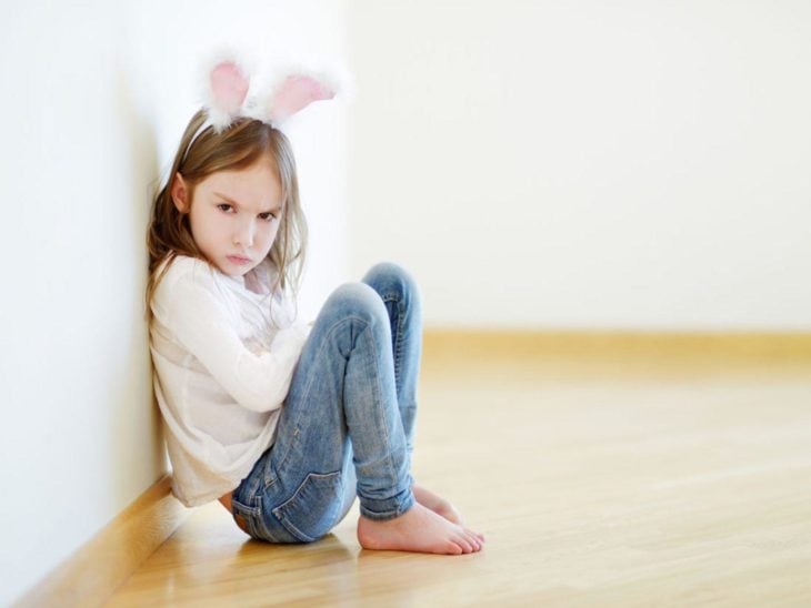 niña con diadema de orejas de conejo sentada de brazos cruzados con gesto de molestia