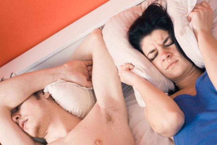 Mujer tapándose los oídos con la almohada porque su pareja está roncando