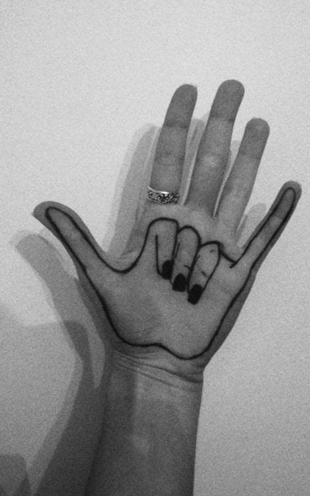 Chica con un tatuaje en las palmas de las manos en forma de manos haciendo la señal de rock