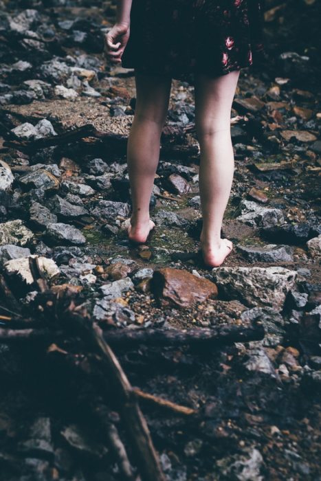 piernas de una mujer que camina por un arroyo con piedras
