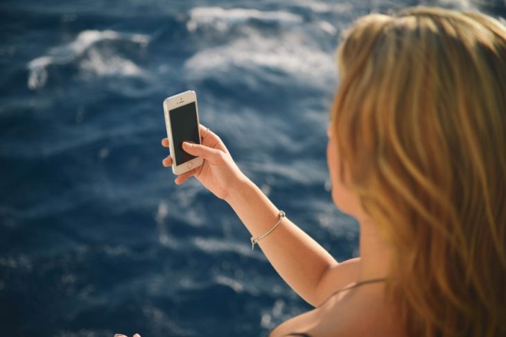 una toma desde atrás de una mujer que está frente al mar y tiene un teléfono celular en su mano