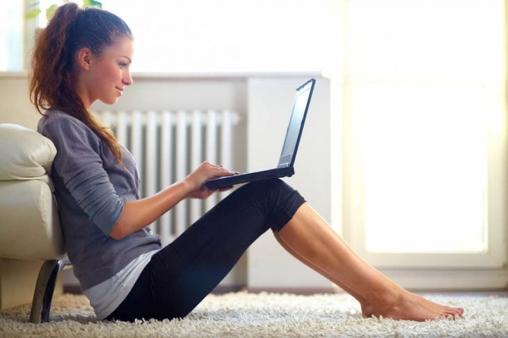 una mujer sentada en la alfombra con la computadora sobre las rodillas