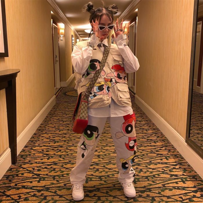 Cantante Billie Eilish posando para una foto mientras está en el pasillo de un hotel usando un traje de las chicas superpoderosas