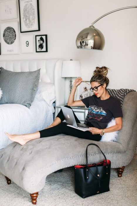 Chica sentada en un sofá con su laptop en las piernas y el bolso en el piso 