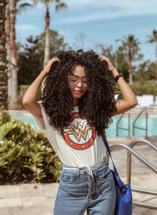 Chica afroamericana con cabello café, chino, esponjado y largo, con blusa de La mujer maravilla