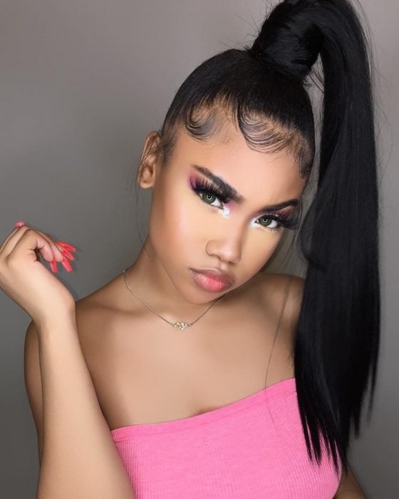 Chica afroamericana con maquillaje rosa, pestañas postizas, con peinado de cola de caballo alta, lacia y baby hairs peinados