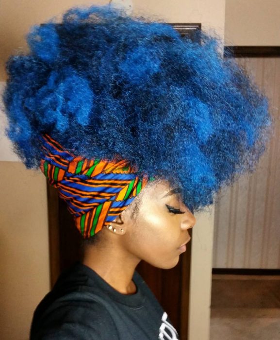 Chica afroamericana con cabello chino, esponjado, de color azul, peinado con una bandana o paliacate