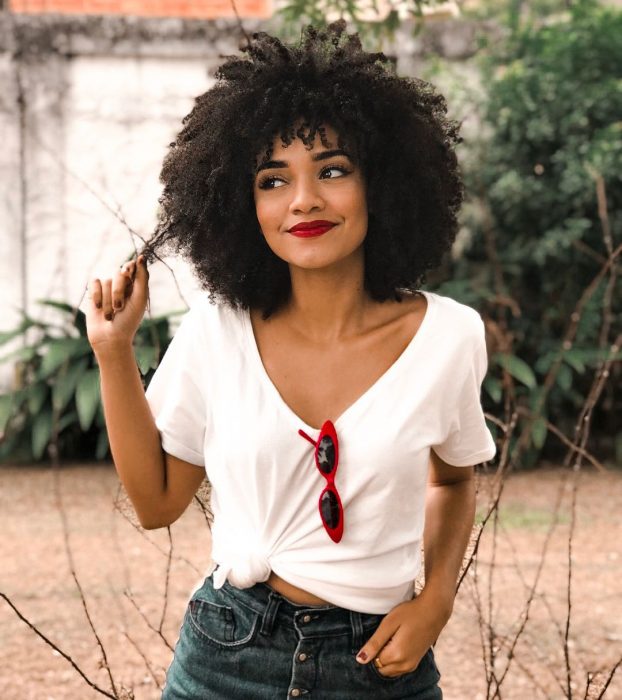 Chica afroamericana sonriendo agarrándose el cabello chino y esponjado