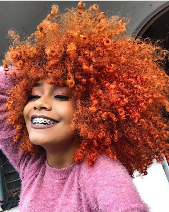 Chica afroamericana con cabello chino afro teñido de anaranjado, con brackets