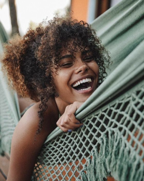 Chica afroamericana de cabello café y chino, riéndose en hamaca 