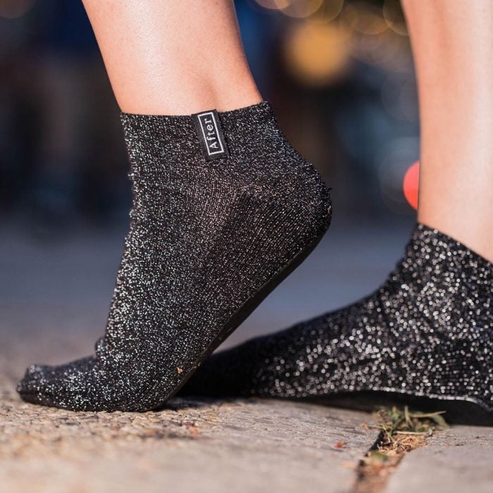 Mujer usando unos calcetines de color negro con brillos diseñados exclusivamente para caminar después de quitarte los tacones 