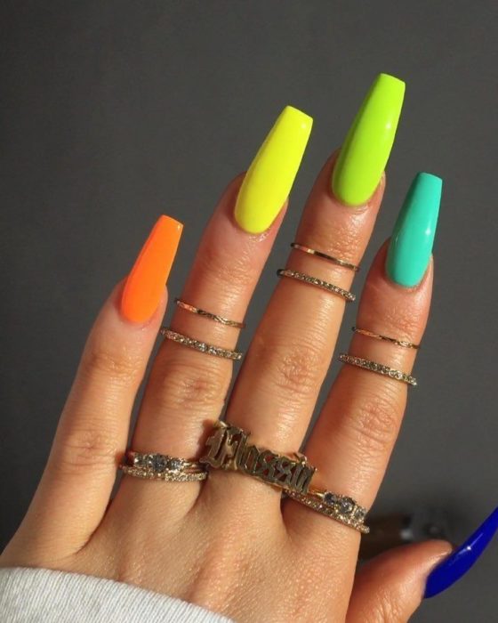 Manos de una mujer con las uñas pintadas en colores neón en amarillo, naranja y verde 