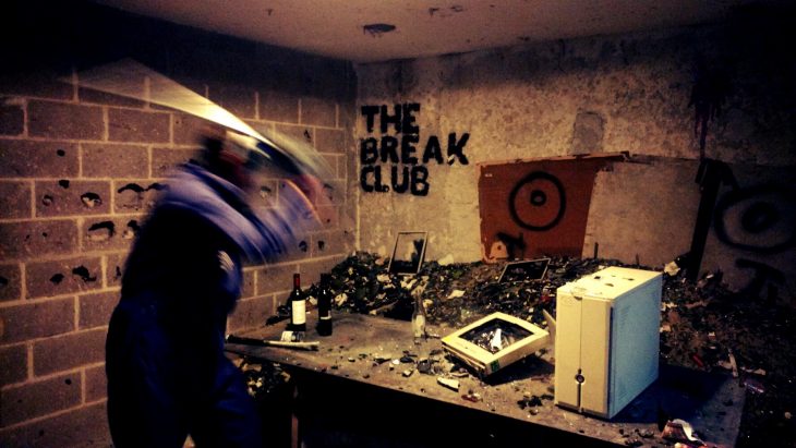 un hombre golpea artículos electrónicos sobre una mesa, en la pared un letrero dice The Break Club