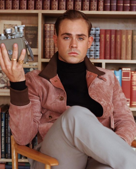 Actor Dacre Montgomery sentado en una biblioteca con saco rosa