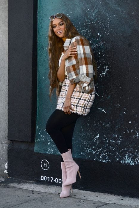 Tyra Banks recargado en una pared modelando sus botas rosas