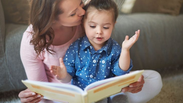 Una mujer besa a su hija en la frente mientras la niña ve un libro que su madre sostiene
