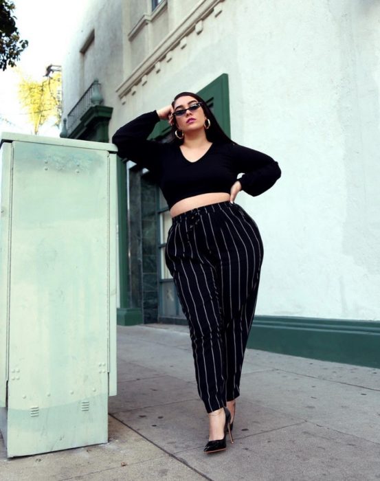 Atuendos para chicas plus size; chica con crop top y pantalón negro de rayas verticales