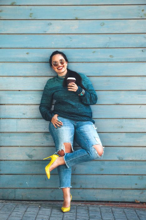 Atuendos para chicas plus size; chica sonriendo con suéter verde, jean y zapatillas amarillas