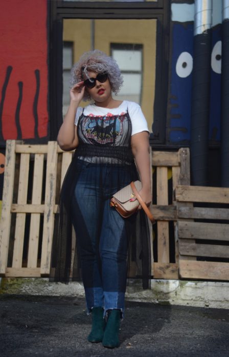 Atuendos para chicas plus size; chica de cabello corto, chino y de color lila, con vestido tranpsarente arriba de blusa básica y jean