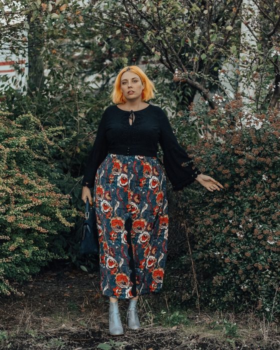 Atuendos para chicas plus size; chica de cabello corto y anaranjado, con pantalón floreado en el jardín