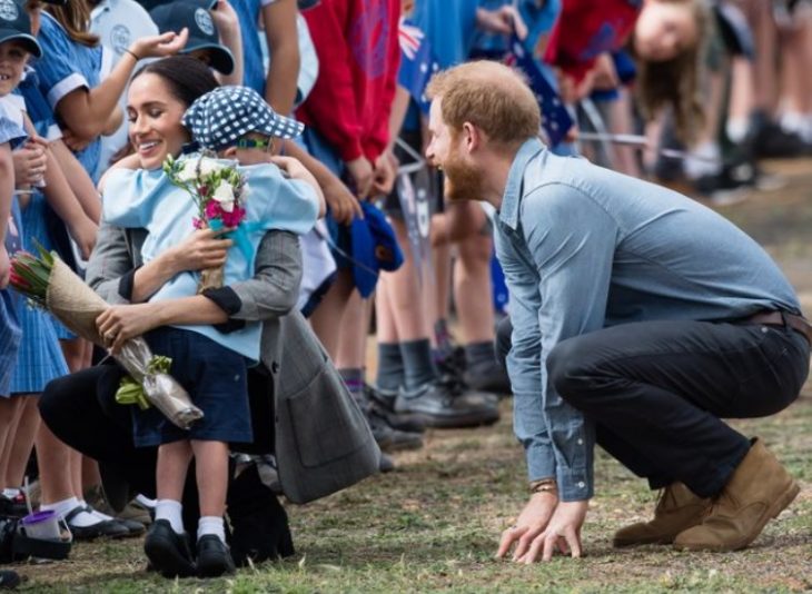 Meghan Markle abraza a un niño mientras Harry a su lado en cuclillas le hace cariños