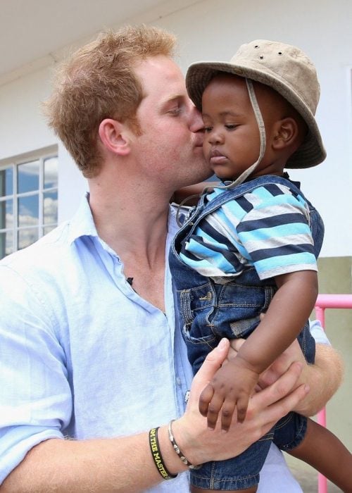 Príncipe Harry con un niño africano en los brazos a quien besa en la mejilla