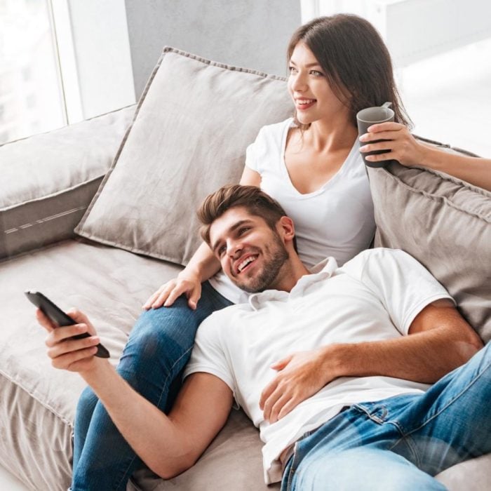 Una pareja en un sofá, el hombre tiene un control de televisión