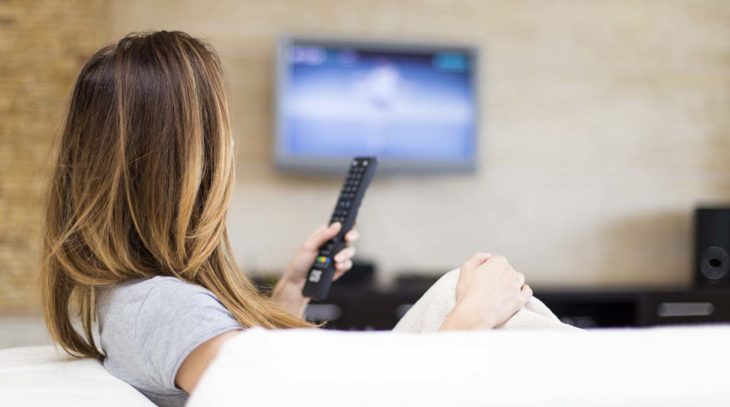 vista de atrás una mujer con un control y una pantalla al frente de ella encendida