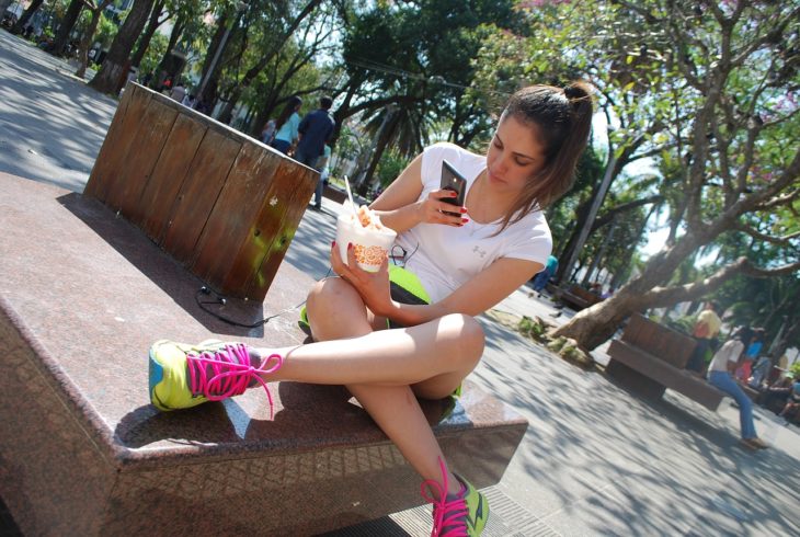 una mujer con ropa deportiva sentada en un banco en un parque revisando su celular