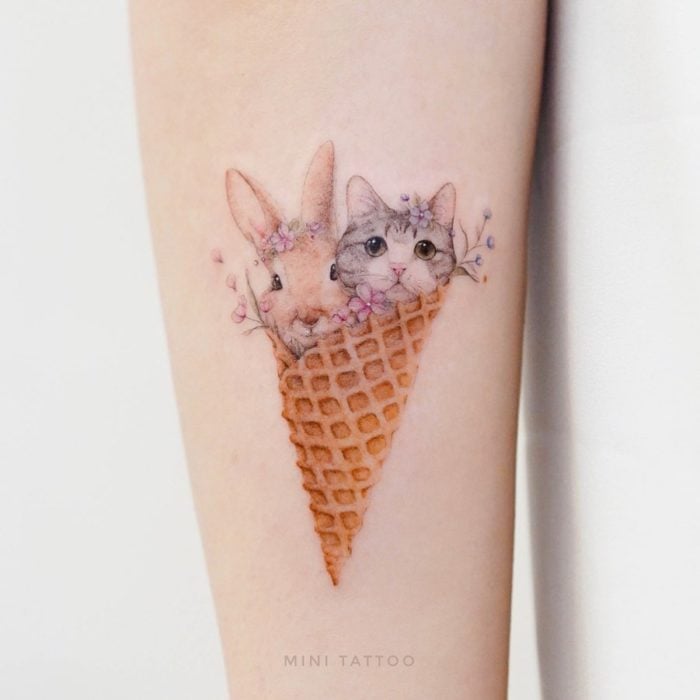 Tatuadora china, Mini Lau; tatuaje pequeño y femenino con colores pastel de un conejo y un gato en un cono de helado