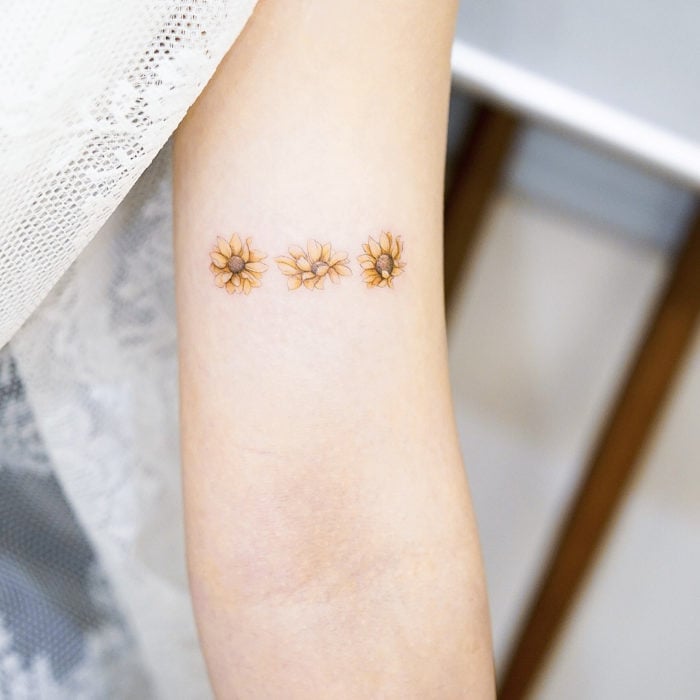 Tatuadora china, Mini Lau; tatuaje pequeño y femenino con colores pastel de girasoles en el brazo