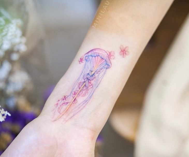 Chinese tattoo artist, Mini Lau;  Small, feminine tattoo with pastel colors of pink jellyfish with blue and cherry blossoms
