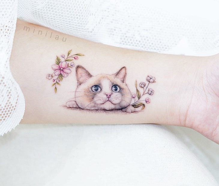 Tatuadora china, Mini Lau; tatuaje pequeño y femenino con colores pastel de gato siamés con flores rosas y lilas