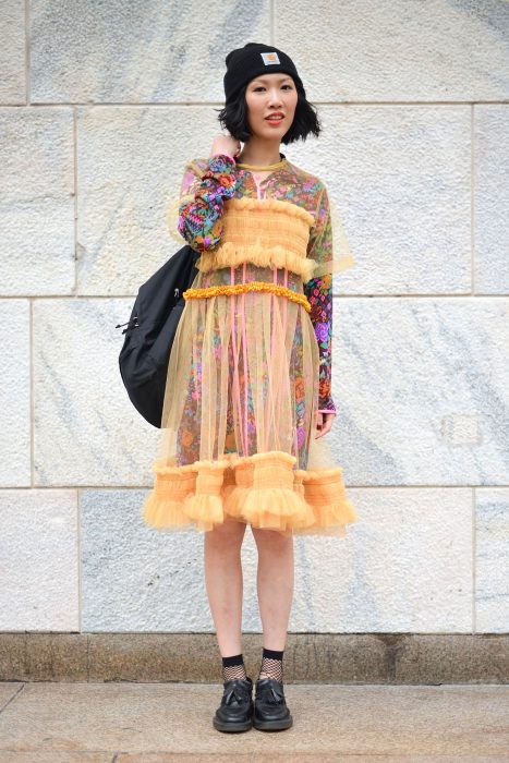 Moda japonesa harajuku; chica con vestido floreado debajo de vestido transparente anaranjado, con gorra y mochila