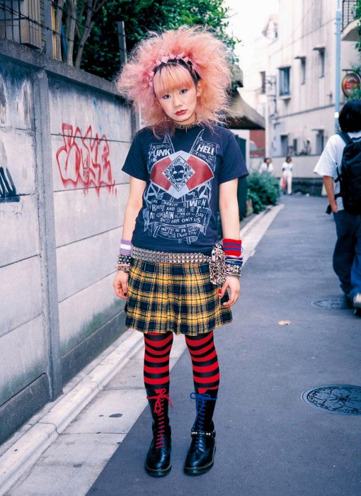 Moda japonesa harajuku; chica con estilo punk de cabello esponjado y rosa, falda de estampado de cuadros y medias de rayas rojas