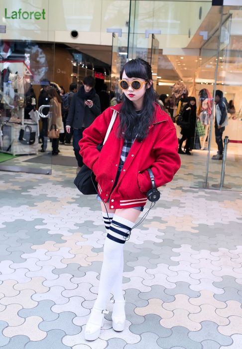 Moda japonesa harajuku; chica de cabello negro y largo, con lentes redondos, chaqueta de equipo de fútbol, zapatos de plataforma y calcetas largas