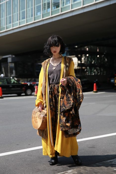 Moda japonesa harajuku; mujer con ropa en capas, gabardina amarilla y bolsa de madera