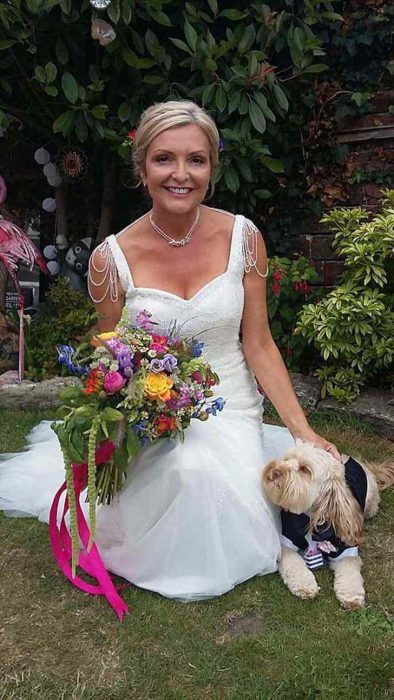 Mujer usando un vestido de boda blanco mientras posa para una sesión de fotos acompañada de su perro