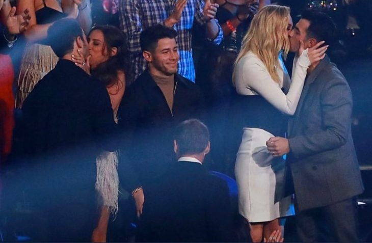 Nick Jonas en medio de sus hermanos mientras ellos besan a sus esposas