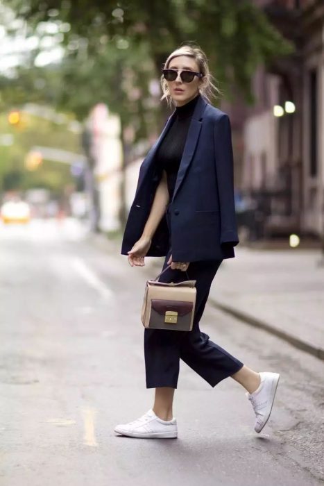 Chica usando un traje de color azul, bolso transparente y tenis de color blanco 