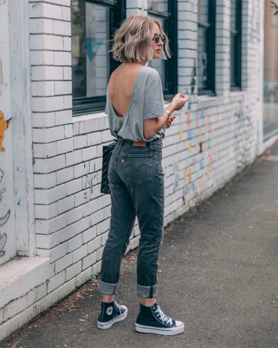 Chica usando jeans con converse y blusa de escote en la espalda de color gris 